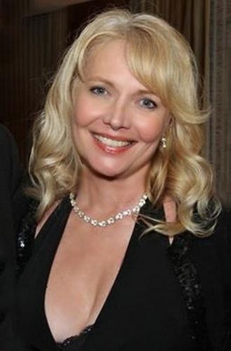 Cindy Morgan smiling while wearing a black blouse, earrings, and necklace