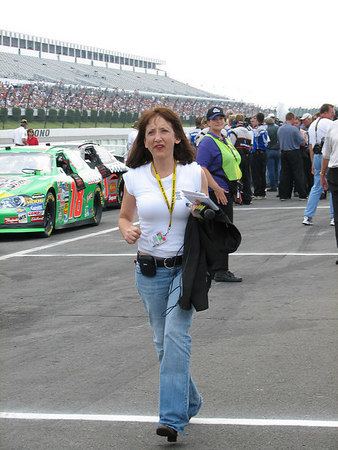 Claire B. Lang hurriedly walking during a racing event, bringing her interview equipment and wearing a white shirt.