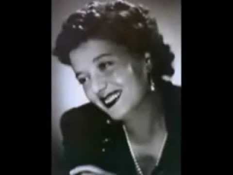 Clara Petacci smiling while looking at something while wearing a blouse, pearl necklace, and earrings