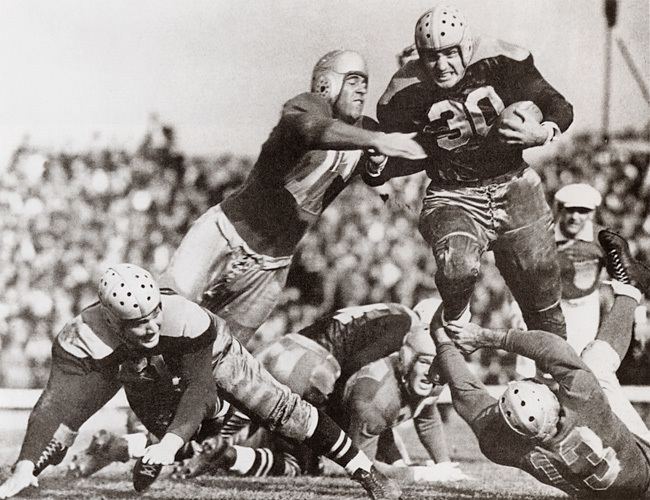 Clarke Hinkle of the Green Bay Packers rushes the ball while two defenders try to tackle him.