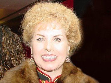 Claudia Islas smiling while wearing a brown fur jacket, black and red blouse, and earrings