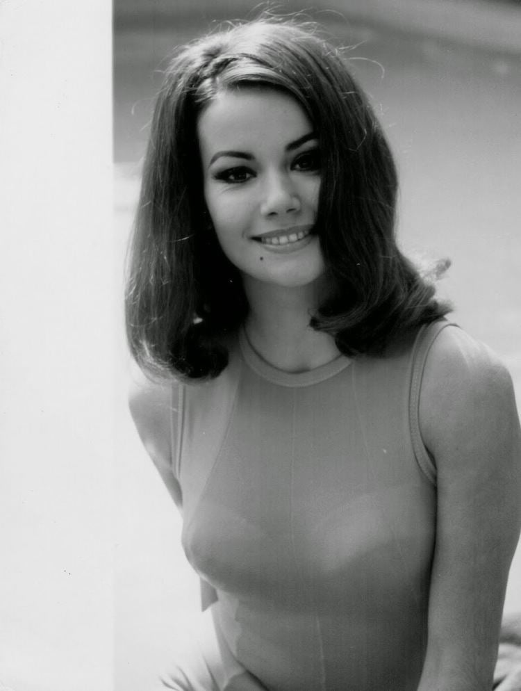 Claudine Auger smiling with shoulder-length wavy hair while wearing a sleeveless top