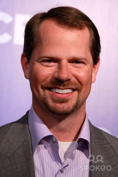 Coby G. Brooks smiling while wearing a gray coat and violet long sleeves