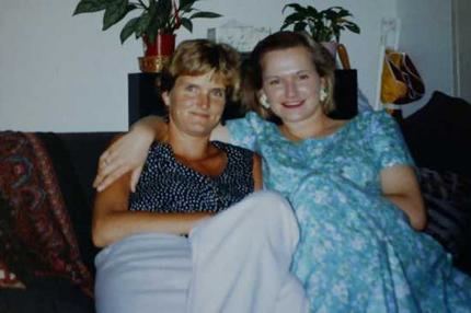 Cornelia Rau smiling, with blonde hair and wearing a blue dress with a woman with short blonde hair.