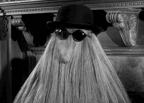 Cousin Itt smoking with floor-length blonde hair while wearing black sunglasses and a hat