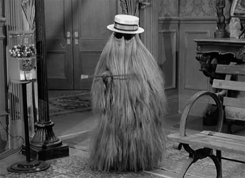 Cousin Itt cousin twirling a stick with floor-length blonde hair while wearing black sunglasses and a hat