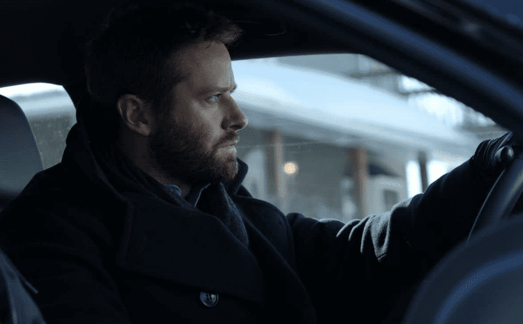 Armie Hammer driving the car while wearing a black trench coat in a scene from the 2021 crime thriller film, Crisis