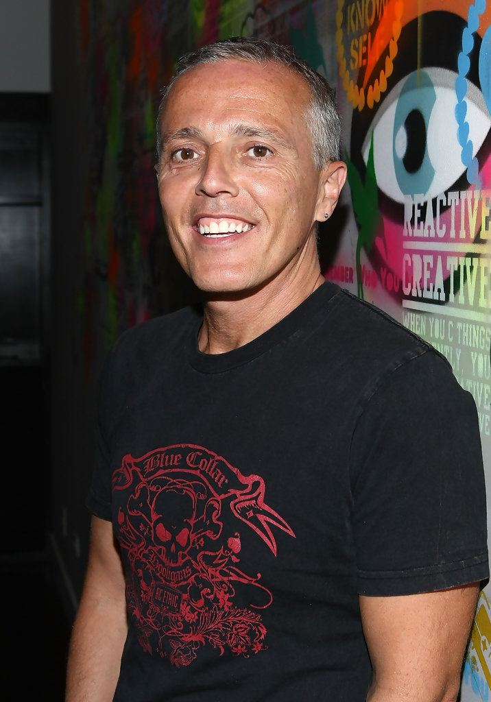 Curt Smith with a big smile and gray hair while wearing a black t-shirt with a skull and blue collar print