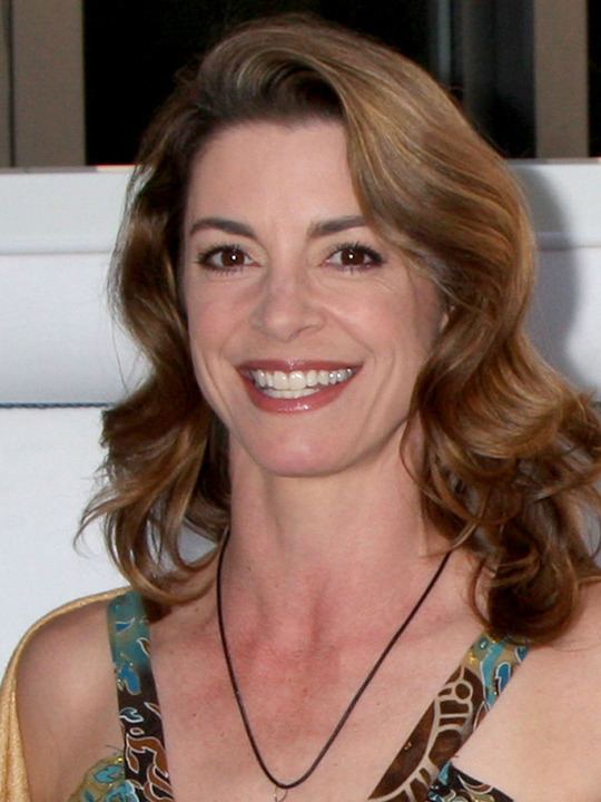 Cynthia Gibb smiling with wavy blonde hair and wearing a colored sleeveless blouse, and black necklace