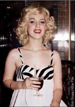 Cyrinda Foxe smiling and holding a goblet while wearing black and white dress