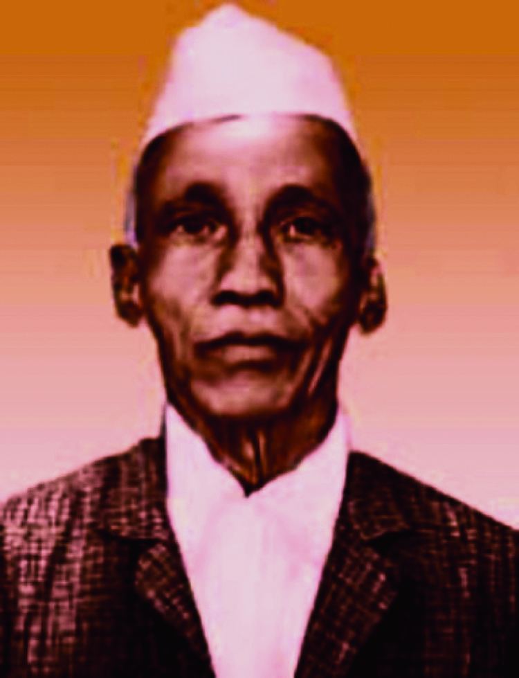 Portrait of D. R. Kaprekar wearing a white cap, brown checkered coat, and white long sleeves