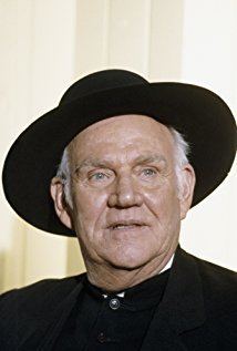 Dabbs Greer looking afar with a serious face while wearing a black hat and a black long sleeve under a black coat