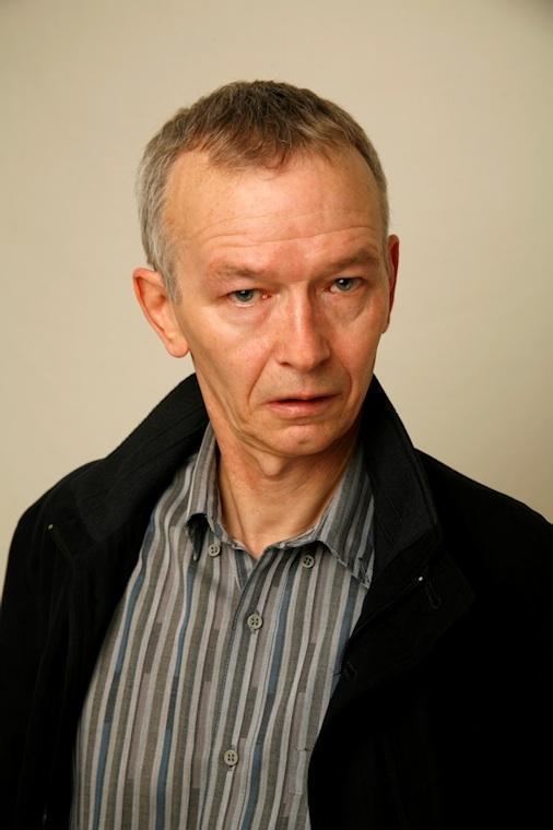 Dai Bradley looking serious, wearing a stripe buttoned shirt under a black coat
