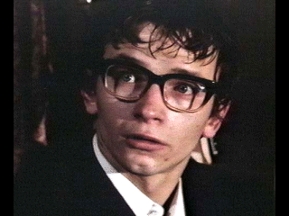 Dai Bradley as Arthur Dyson looking terrified in the 1978 film "Absolution" and wearing a white shirt under a black coat and eyeglasses