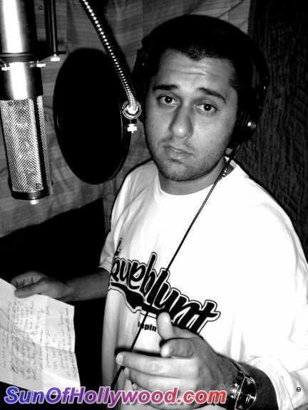 Damizza looks serious inside a recording studio while holding a piece of paper and wearing a headset, a white shirt with black prints, a watch, and a necklace