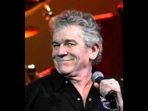 Dan McCafferty smiling while holding a microphone and wearing black long sleeves