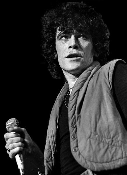 Dan McCafferty looking afar while holding a microphone and wearing a t-shirt and vest