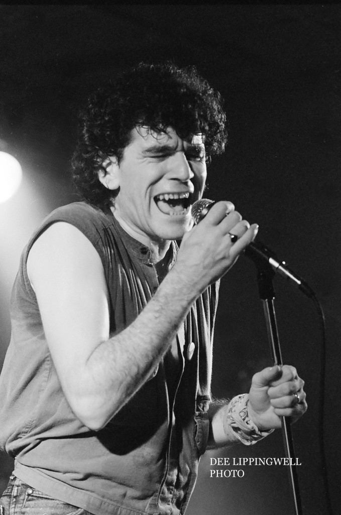 Dan McCafferty singing while holding the microphone and wearing a sleeveless jacket and ring