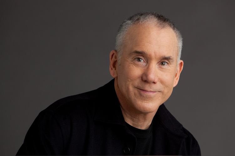 Dan Millman smiling while wearing a black shirt and black coat