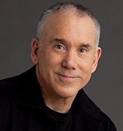 Dan Millman smiling while wearing a black shirt and black coat