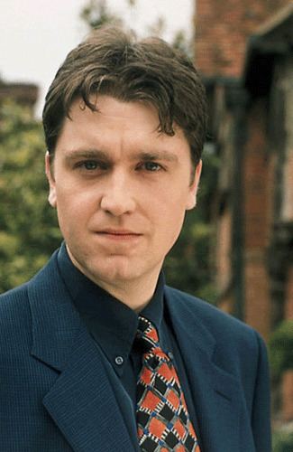 Daniel Casey wearing a dark blue coat, black long sleeves, and necktie