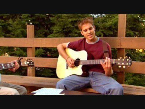 Daniel Letterle while playing a guitar wearing a red shirt and denim pants in a movie scene from "Camp"