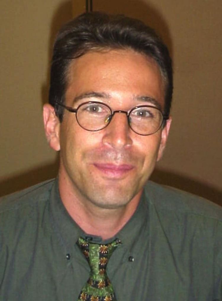 Daniel Pearl smiling while wearing eyeglasses, green long sleeves, and necktie