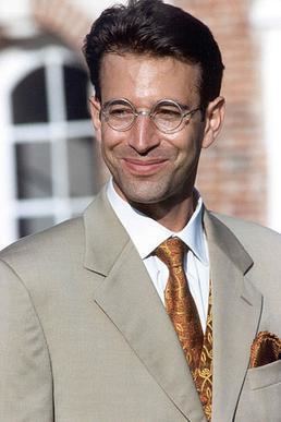 Daniel Pearl smiling while wearing a grayish-brown coat, white long sleeves, gold necktie, and eyeglasses