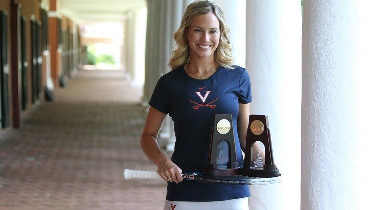 Danielle Collins in her blue shirt with V symbol while holding her racket and trophies