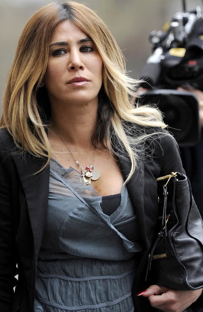 Danielle McGuire with a serious face while carrying a black bag, with blonde hair, wearing a necklace, black blazer over a gray blouse, and black top.