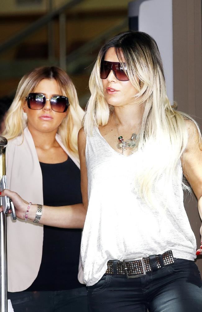 Danielle and Brittany Mcguire with serious faces, both wearing sunglasses and with blonde hair. Dannielle wearing a white sleeveless top and black jeans while Brittany wearing a white blazer over a black shirt.