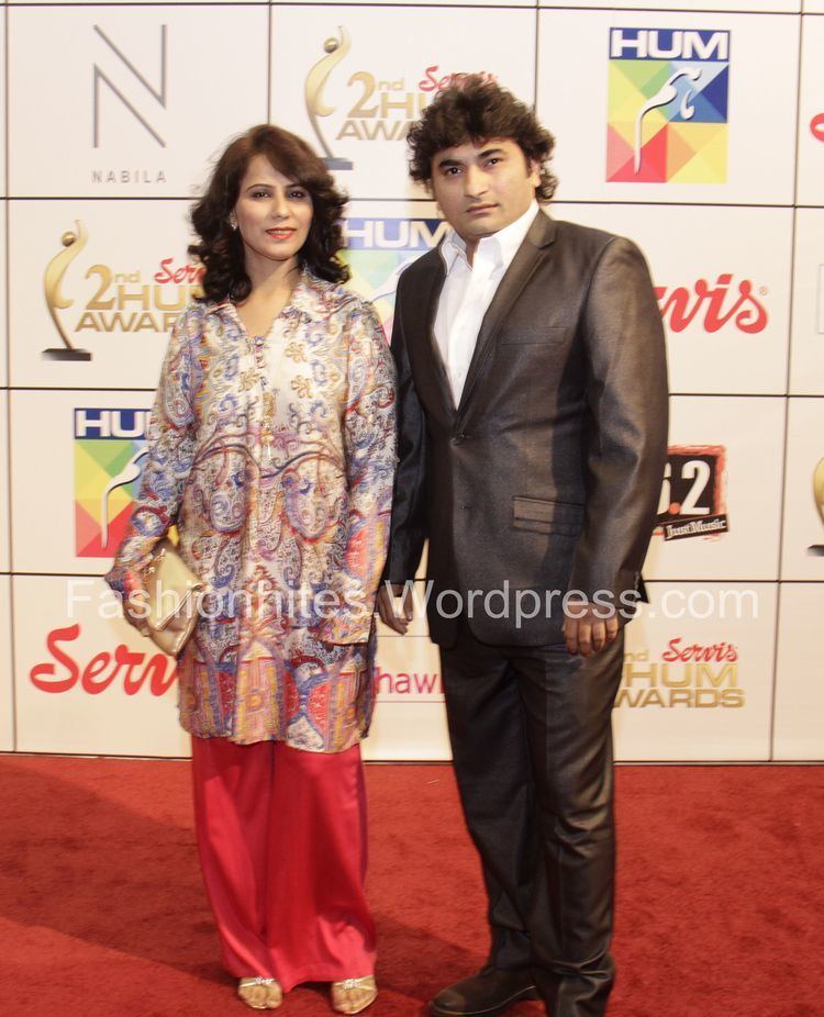 Danish Nawaz Anila wearing a black coat, white long sleeves, and black pants while his wife wearing white and blue long sleeves and orange pants