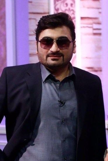 Danish Nawaz smiling while wearing a black coat, shades, and blue long sleeves