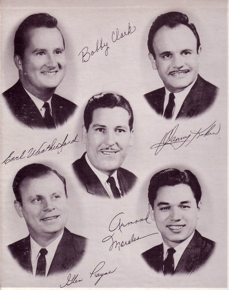 Danny Koker’s father in the middle while smiling and wearing coat, long sleeves and neck tie