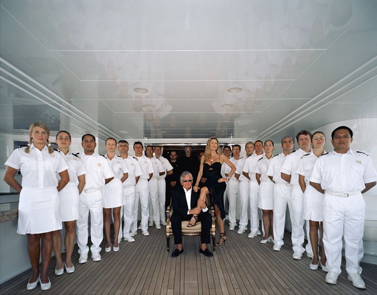 Darwin Deason sitting on the chair and holding Katerina Panos Deason's legs while their crew and security forces are standing beside them