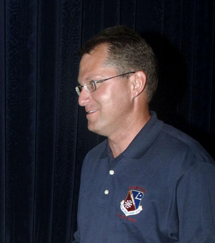 Dave Pelzer speaking to Airmen while visiting troops in Southwest Asia while wearing eyeglasses and a blue polo shirt with a patch of logo