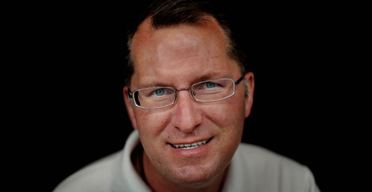 Dave Pelzer smiling while wearing a light gray polo shirt and eyeglasses