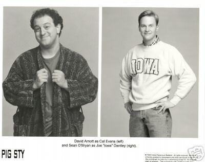 On the left, David Arnott with a tight-lipped smile while holding his black robe, with curly hair, and wearing a gray shirt. On the right, Sean O'Bryan with a tight-lipped smile while his hands are on his waist, wearing a white jacket over checkered long sleeves and jeans.
