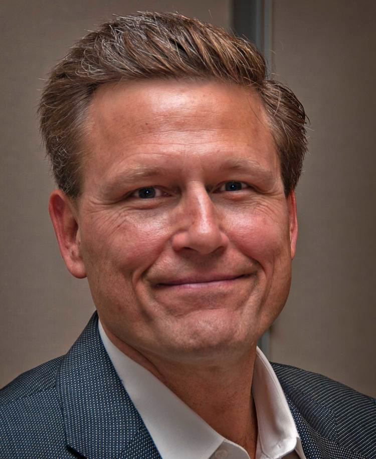 David Baldacci with a tight-lipped smile while wearing a black dotted coat and white long sleeves