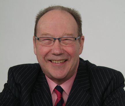 David Barby smiling while wearing a black striped coat, pink long sleeves, maroon necktie, and eyeglasses