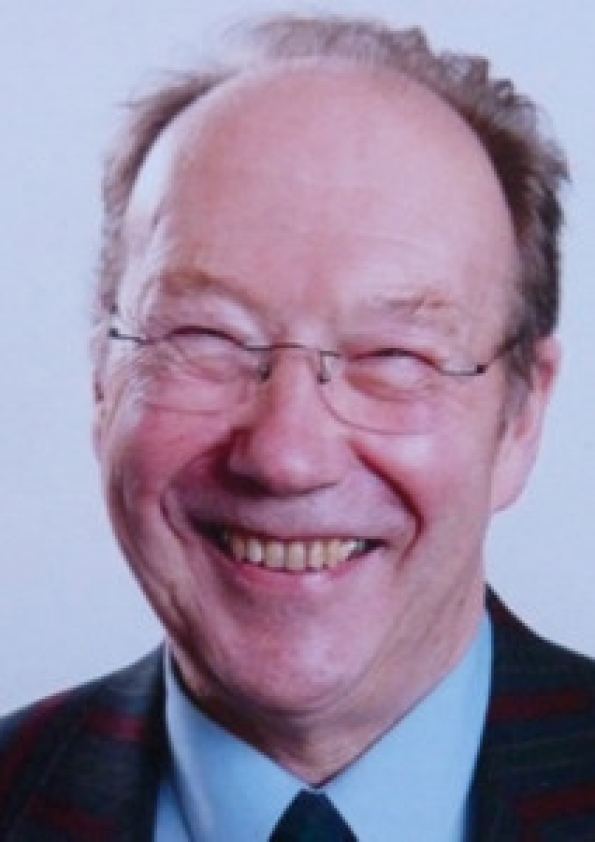 David Barby smiling while wearing a black coat, blue long sleeves, black necktie, and eyeglasses