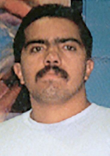 David Barron Corona with serious face and mustache while wearing a white t-shirt