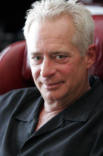 David Bradley smiling and with white hair, wearing a black polo shirt.