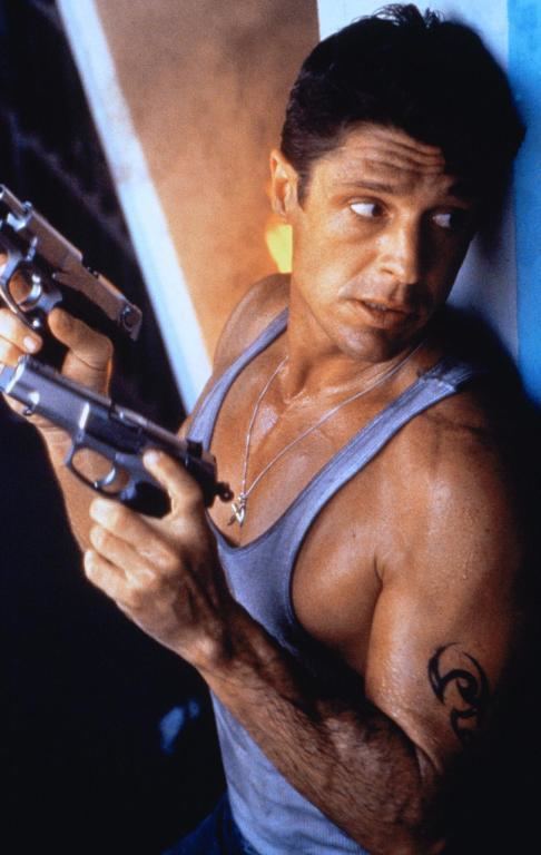 Scene from Cyborg Cop II, a 1994 American action film starring David Bradley as Jack Ryan wearing a sando, a necklace while holding guns.
