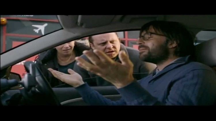 David Earl talking to a man and woman with hand gestures and he is inside the car, with mustache and beard, while wearing eyeglasses and blue long sleeve shirt