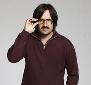 David Earl holding his eyeglasses with a serious face and mustache while wearing a brown long sleeve shirt