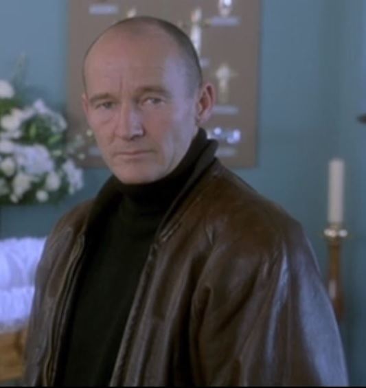 David Hayman as Michael Walker in a scene from Trial & Retribution, 1997 wearing a black shirt under a brown leather jacket.