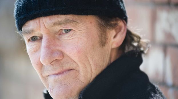 David Hayman looking at something while wearing a black ball cap and black coat.