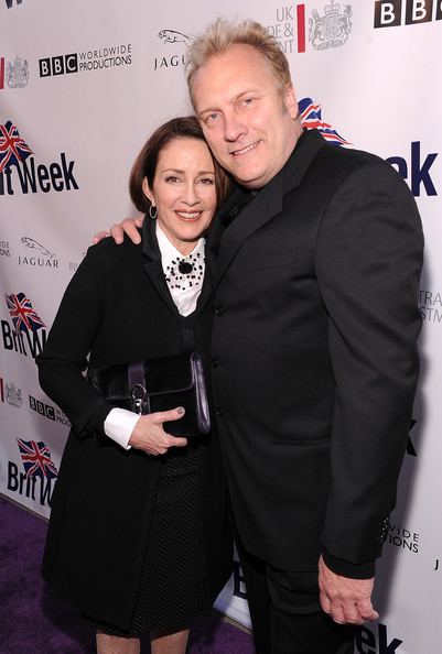 David Hunt smiling and wearing a black suit together with Patricia Heaton wearing a black and white dress while carrying a black bag.