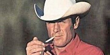 David McLean is serious, lighting up the cigarette in his mouth with his left hand and right hand covering, has black hair, wearing a white cowboy hat and red polo.